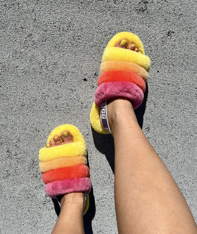 Feet with yellow painted toenails wearing UGG brand Pride Fluff Yeah Slides in 'Pride Rainbow Yellow'