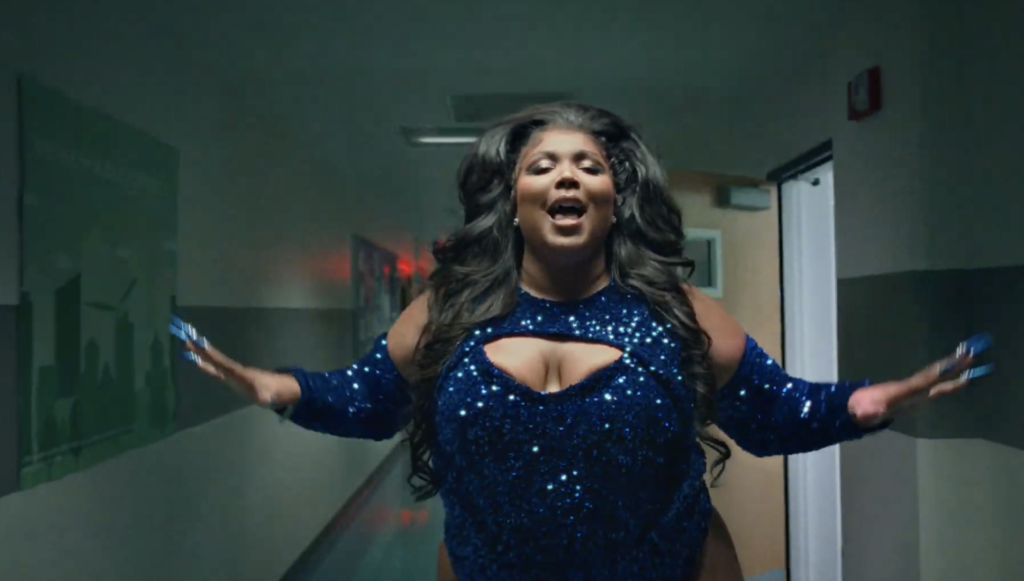 Artist Lizzo singing in a hallway wearing a sequined blue outfit.